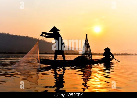 Asia fisherman net utilizzando sulla barca di legno netto di colata il tramonto o l'alba nel fiume Mekong - Silhouette fisherman barca con sfondo di montagna la vita pe Foto Stock