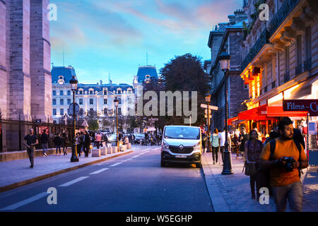I turisti e i locali di godersi una serata fuori a negozi e caffetterie sulla Ile de la Cite isola di fronte la Cattedrale di Notre Dame a Parigi, Francia Foto Stock