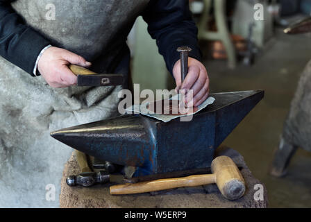 Vecchio smith è chieseling un foglio di rame in officina, rendendo pattern Foto Stock