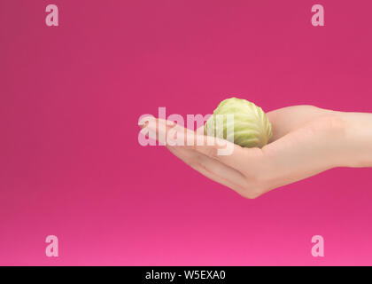 Mano femmina trattiene il cavoletto di Bruxelles babe su uno sfondo rosa, il concetto di una corretta alimentazione e salute, dietology, isolat, copia spazio, vitamina defic Foto Stock