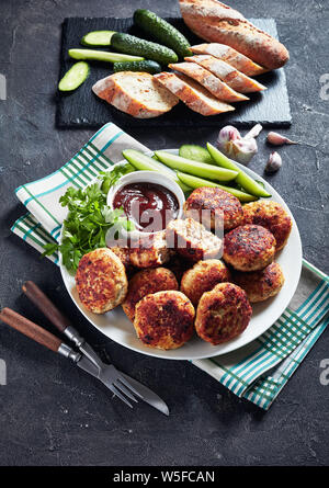 Polacco polpette di carne serviti con fette di cetriolo e salsa barbecue su una piastra bianca su una tabella di calcestruzzo con fette di baguette francese, vista verticale fr Foto Stock