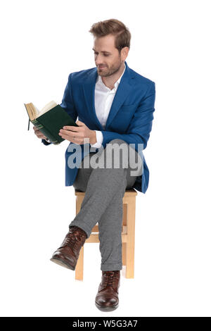 Focalizzato Casual guy leggendo un libro seduti con le gambe incrociate e indossa una tuta bianca su sfondo per studio Foto Stock