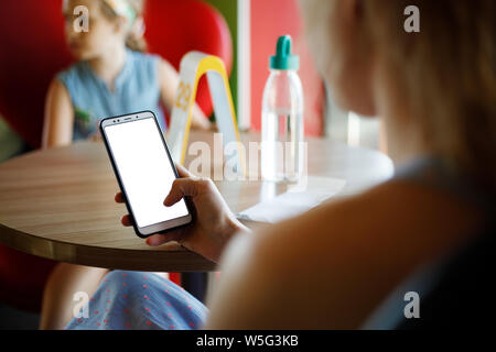 Mockup immagine di donna di mani white telefono cellulare con schermo vuoto in cafe. Foto Stock