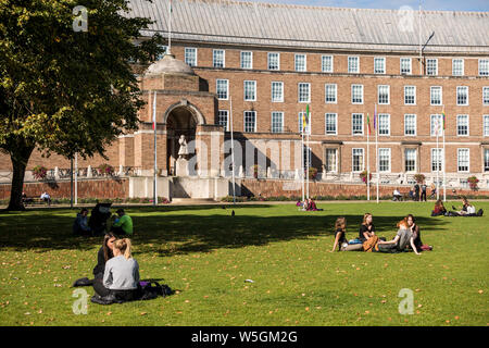 I giovani seduti su erba a College Green avente conversazione, Bristol, Regno Unito Foto Stock