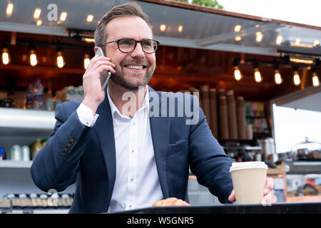 Imprenditore maturo tenendo chiamata sul cellulare seduti al Outdoor Coffee Shop Foto Stock