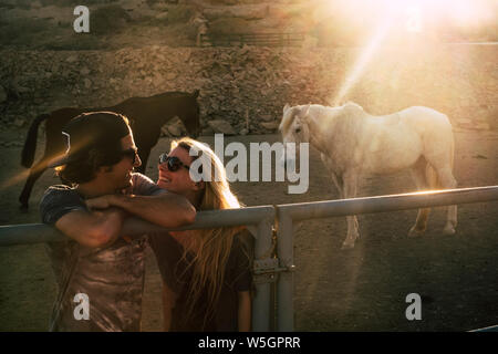 Giovane gente allegra coppia felice scoperta in rapporto romantico con i cavalli e del tramonto sullo sfondo - Concetto di stile di vita alternativo per millen Foto Stock