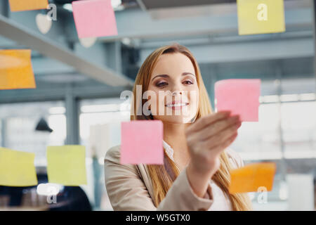 Felice designer note di incollaggio sulla finestra in ufficio Foto Stock