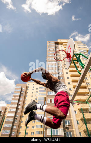 Vista dal basso del giovane africano basketballer in salto gettando la sfera nel carrello Foto Stock