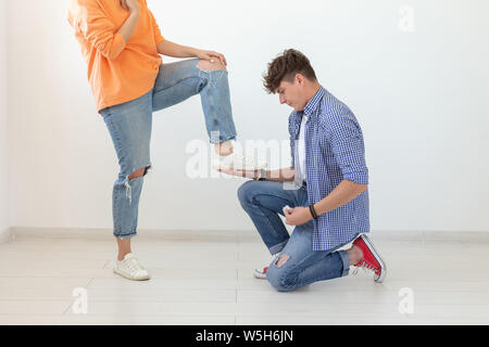 Giovane uomo è in ginocchio e riverenti legatura di lacci delle scarpe per il suo dominatore donna non identificato in posa su uno sfondo bianco. Nozione di posizione dominante Foto Stock