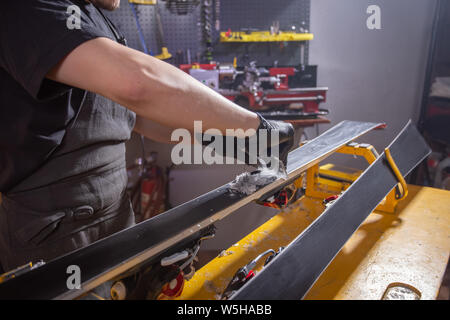 Lavoro e concetto di riparazione - un uomo con le mani in mano la riparazione sci mediante sfregamento di una paraffina Foto Stock