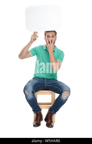 Seduto sconvolto l uomo in verde Polo shirt contiene un discussione vuoto cloud fino in aria su sfondo bianco Foto Stock