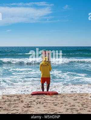 Un bagnino di pattuglia sulla spiaggia durante il periodo estivo è la messa in atto di un cartello di avvertimento per i nuotatori di avventurarsi nell'oceano Foto Stock