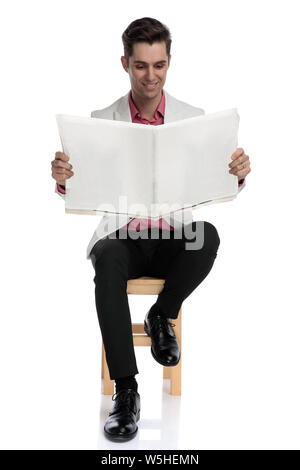 Elegante giovane uomo seduto su una sedia e legge un giornale o sfondo wite Foto Stock