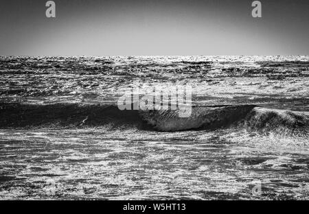 Bellissimo scatto di onde di mare con cielo limpido nel sfondo in bianco e nero Foto Stock