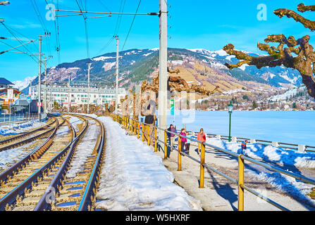 ZELL AM SEE, Austria - 28 febbraio 2019: il paesaggio con la ferrovia, inverno Elisabeth Park, congelati lago Zeller See e luxury Grand Hotel su backgro Foto Stock