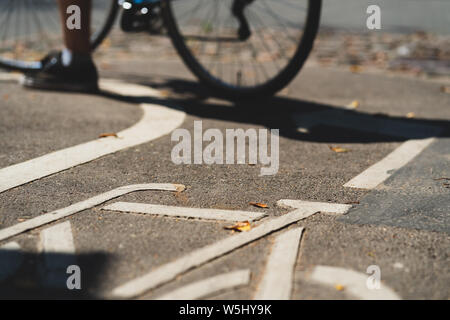 Un ciclista sorge su un percorso in bicicletta con una bicicletta stencil su grigio asfalto con foglie di giallo in estate Foto Stock