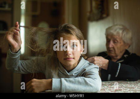 Una vecchia donna trecce una bambina - nipote capelli lunghi. Foto Stock