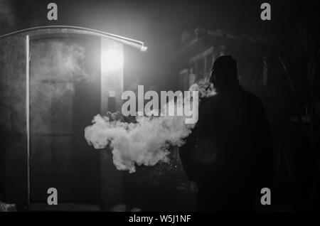 Strano uomo di fumare durante la notte con grande effetto di vapore dalla sigaretta Foto Stock