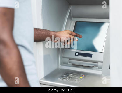 Irriconoscibile uomo africano usando il touch screen su ATM per esterno Foto Stock