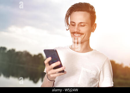 Giovane uomo a camminare vicino alla bellissima baia usando il telefono e cuffie per comunicare con gli amici . buon umore, bella vista Foto Stock