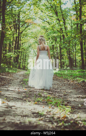 Una ragazzina in abito da solo a piedi nel percorso tra alberi autunnali nella foresta in golden ora atmosfera Foto Stock