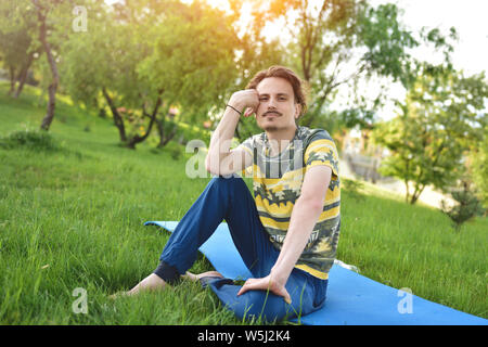 Bel ragazzo elegante gode di natura e sogni su qualcosa seduti nel parco tranquillo vista. estate umore Foto Stock