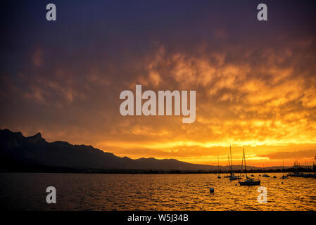 Nuvole illuminate dal sole dopo il tramonto come in un forno in piena di blast con Stockhorn mountain range, il lago di Thun e il Lago di barche a vela sul boe di ancoraggio Foto Stock