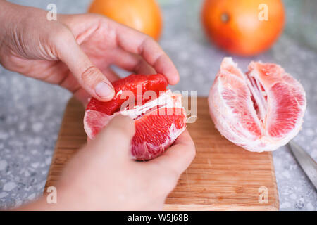 Donna preparando le mani per mangiare pompelmi sul tagliere in cucina domestica. Foto Stock