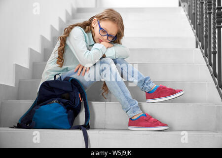 Piuttosto, triste schoolgirl in bicchieri seduto sulla scalinata di scuola, appoggiato sulle ginocchia. Premuto ragazza con lunghi capelli ricci guardando giù, pensando. Foto Stock