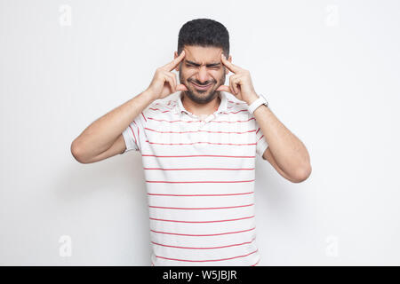 Mal di testa o confution. Ritratto di confusa bello barbuto giovane striped t-shirt in piedi tenendo la sua testa dolorose o pensare. interna studi Foto Stock