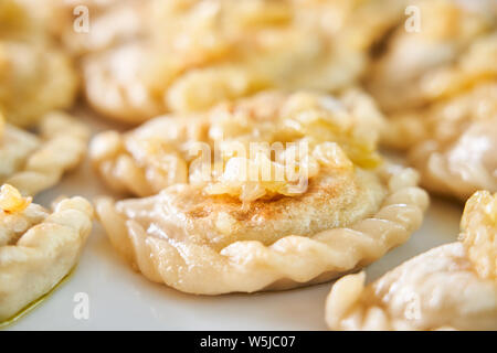 Foto di gnocco fritto con ripieno di carne cosparso con carmelized onion su una piastra bianca Foto Stock