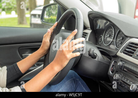 La ragazza con la manicure tiene le mani sul volante della vettura Foto Stock