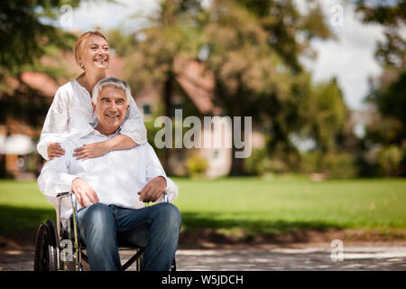 Senior uomo essendo spinto in sedia a rotelle dalla moglie. Foto Stock