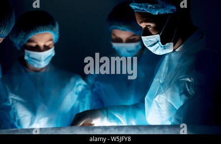 I chirurghi eseguono operazioni chirurgiche nel buio di una sala operatoria Foto Stock