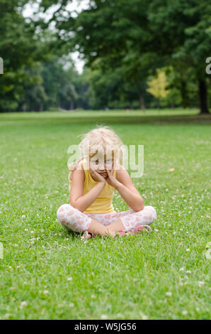 Bella ragazza bionda seduta sul prato Foto Stock