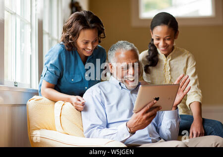 Sorridente uomo senior avendo divertimento utilizzando una tavoletta digitale con la figlia e la nipote. Foto Stock