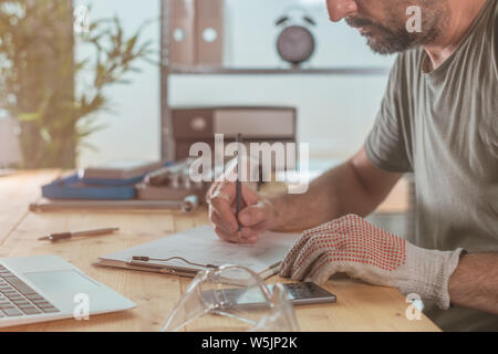 Rendere note del progetto in small business workshop, uomo iscritto Lista da fare alla scrivania Foto Stock