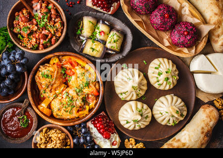 Tradizionale cucina georgiana sfondo. Khinkali, phali, chahokhbili, lobio, formaggio, involtini di melanzane su sfondo scuro, vista dall'alto. Foto Stock