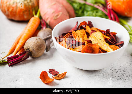 Ciotola di sana chip vegetali da bietole, dolce di patate e carote con ingredienti su uno sfondo bianco. Foto Stock