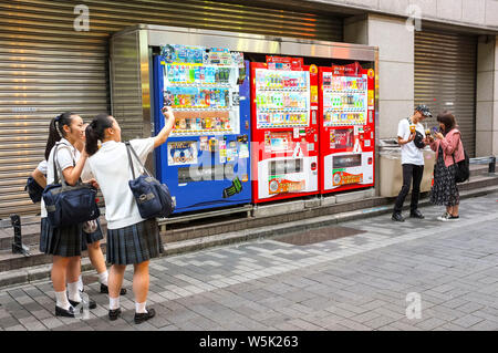 Tre ragazze della scuola tenendo selfies davanti a distributori automatici nel quartiere di Shinjuku a Tokyo in Giappone. Foto Stock