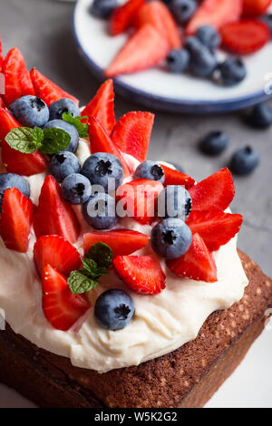 Estate dessert con fragole e mirtilli. Torta di pane con glassa di crema di burro e guarnita con fresche e mature colorata estate frutti e bacche, sel Foto Stock