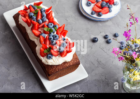 Estate dessert con fragole e mirtilli. Torta di pane con glassa di crema di burro e guarnita con fresche e mature colorata estate frutti e bacche, sel Foto Stock