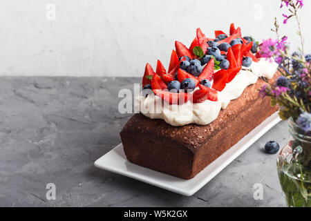 Estate dessert con fragole e mirtilli. Torta di pane con glassa di crema di burro e guarnita con fresche e mature colorata estate frutti e bacche, sel Foto Stock