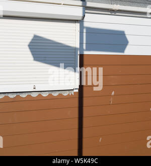 Ombra di direzioni segno cade su un marrone e bianco Beach Hut, direzione segni il punto in direzioni opposte. Foto Stock