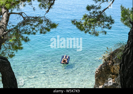 Irriconoscibile turista gode la spiaggia a Brela. La riviera di Makarska in Croazia è famosa per le sue belle spiagge di ciottoli e acqua cristallina. Foto Stock