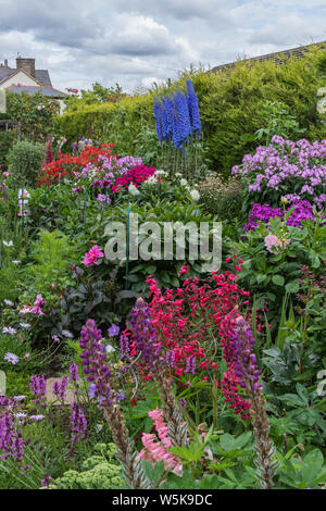 Un giardino inglese in estate. Una stretta fino a una frontiera di piante erbacee perenni in piena fioritura. Foto Stock