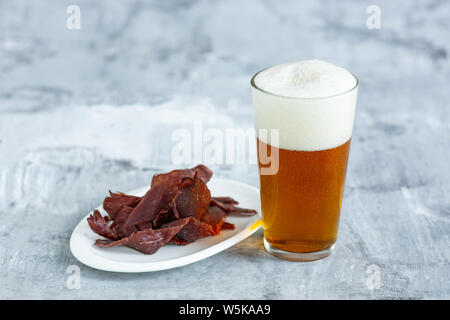 Bicchiere di birra sulla pietra bianca di sfondo della tabella. Drink e snack a base di carne sono preparati per una grande festa. Concetto di bevande, divertente, cibo, celebrando, sale riunioni, Oktoberfest. Foto Stock