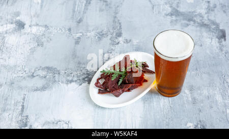 Bicchiere di birra sulla pietra bianca di sfondo della tabella. Drink e snack a base di carne sono preparati per una grande festa. Concetto di bevande, divertente, cibo, celebrando, sale riunioni, Oktoberfest. Foto Stock