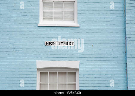 Un 'High Street' segno tra due vecchio stile verniciato bianco finestre a ghigliottina impostato in un dipinto di blu un muro di mattoni Foto Stock