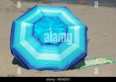 Un colorato a strisce blu ombrellone impostato su di una spiaggia di sabbia. Foto Stock